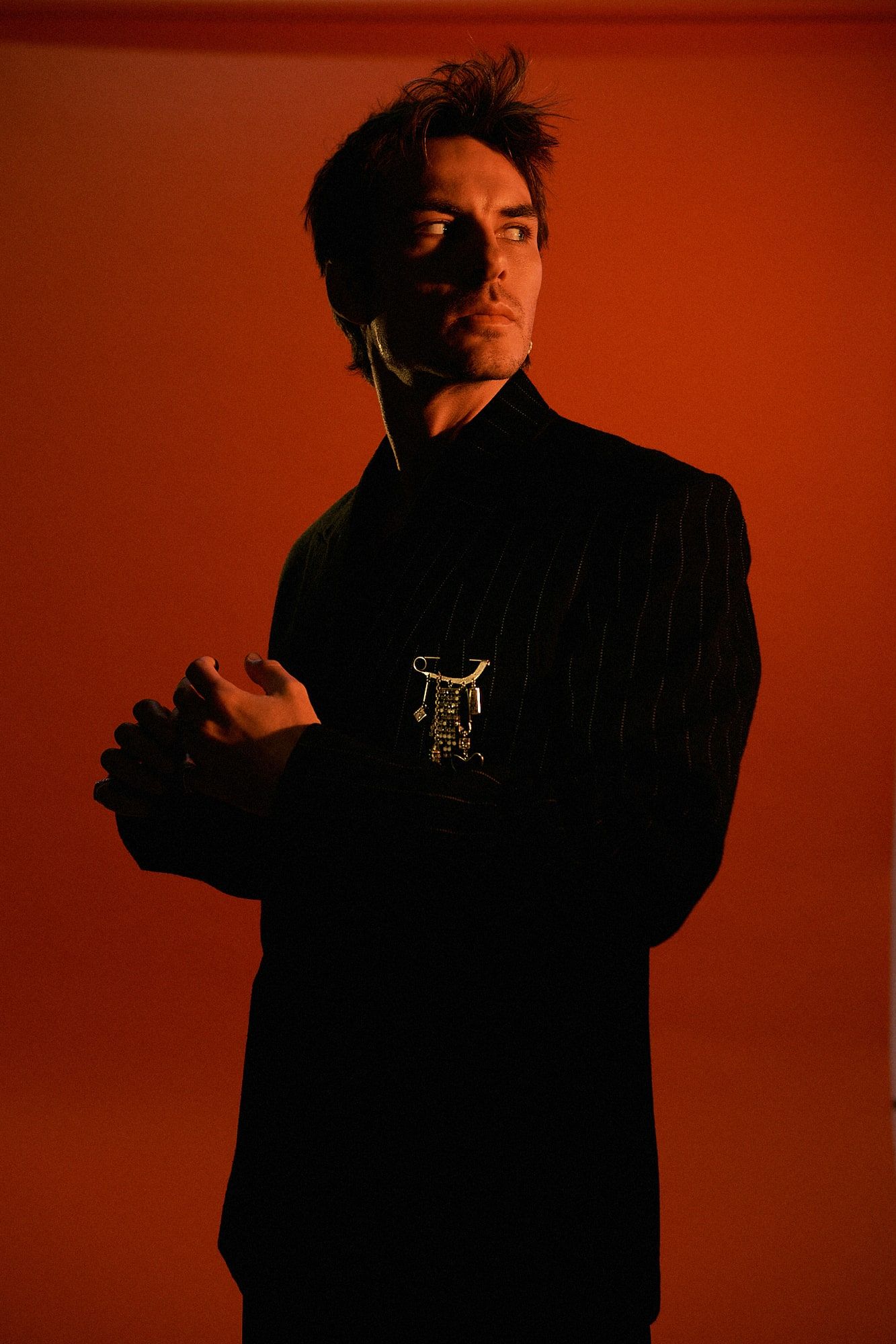 Andrés Koi de traje oscuro sobre fondo rojo, mirando a un lado con las manos entrelazadas